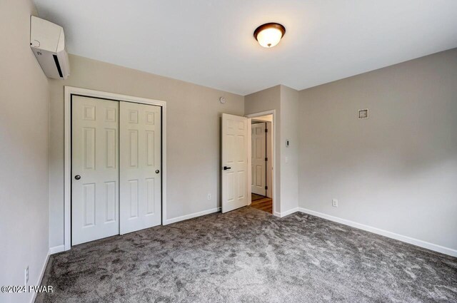 unfurnished bedroom featuring dark colored carpet, a wall mounted air conditioner, and a closet