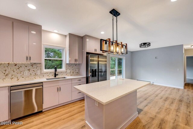 kitchen with sink, light wood-type flooring, appliances with stainless steel finishes, tasteful backsplash, and decorative light fixtures