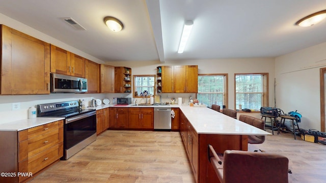 109 Lake Dr, Dingmans Ferry, PA 18328 - kitchen featuring open shelves, a peninsula, appliances with stainless steel finishes, a kitchen bar, and brown cabinets