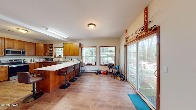 109 Lake Dr, Dingmans Ferry, PA 18328 - kitchen featuring stainless steel appliances, a breakfast bar area, brown cabinetry, light wood-style floors, and a peninsula