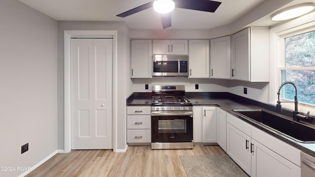 kitchen with appliances with stainless steel finishes, ceiling fan, sink, white cabinets, and light hardwood / wood-style floors