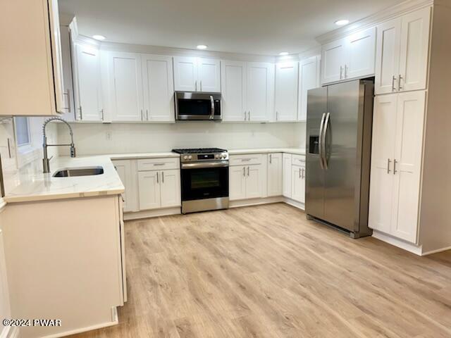 kitchen with light stone countertops, appliances with stainless steel finishes, sink, light hardwood / wood-style floors, and white cabinetry