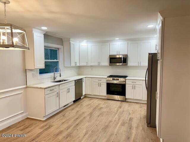 kitchen with light wood-type flooring, stainless steel appliances, white cabinetry, and hanging light fixtures