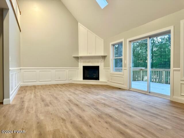 unfurnished living room featuring lofted ceiling with skylight and light hardwood / wood-style flooring