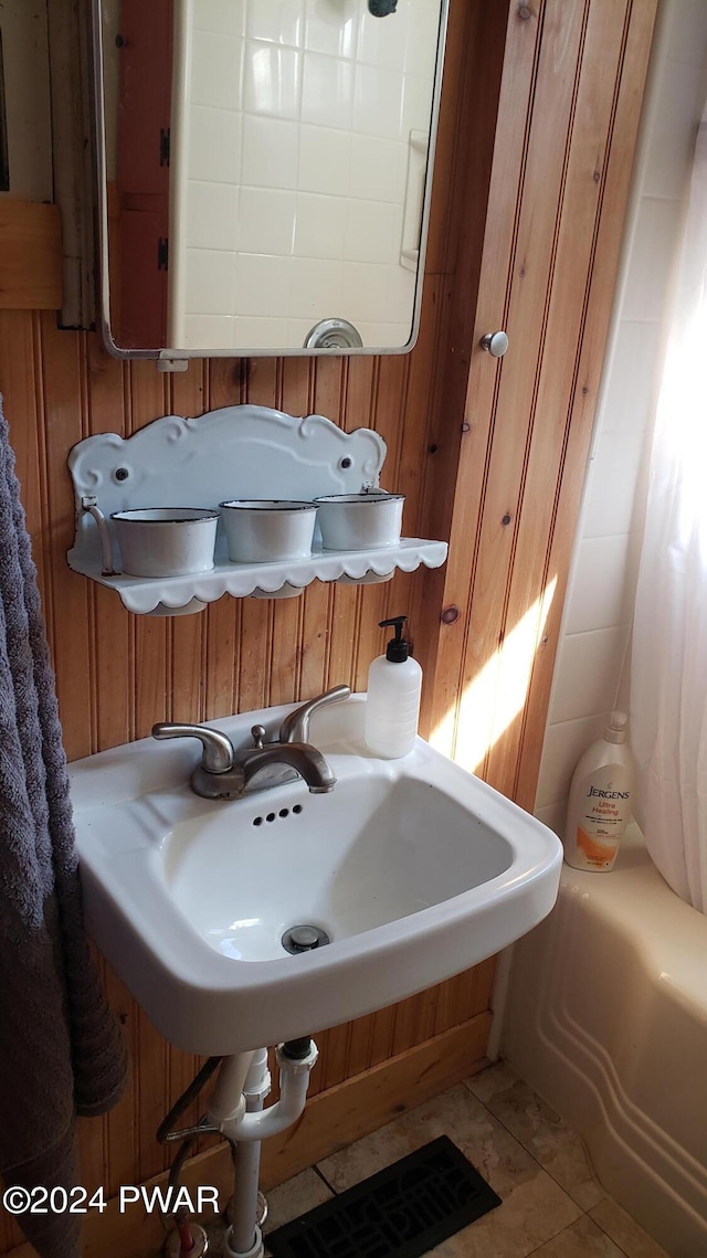 bathroom with wood walls, shower / bath combo with shower curtain, sink, and tile patterned flooring