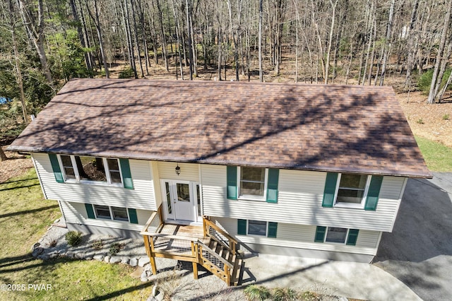 raised ranch featuring a view of trees, a shingled roof, and a front yard