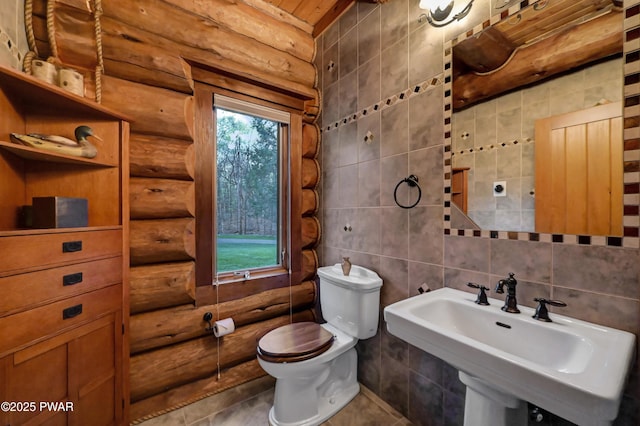 bathroom featuring a sink, rustic walls, toilet, and tile walls