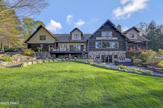 back of property featuring a yard, a chimney, a hot tub, and a balcony