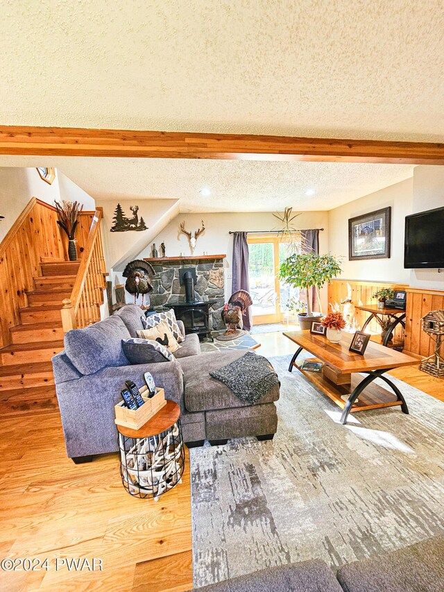 living room featuring a wood stove, beamed ceiling, wood-type flooring, and a textured ceiling