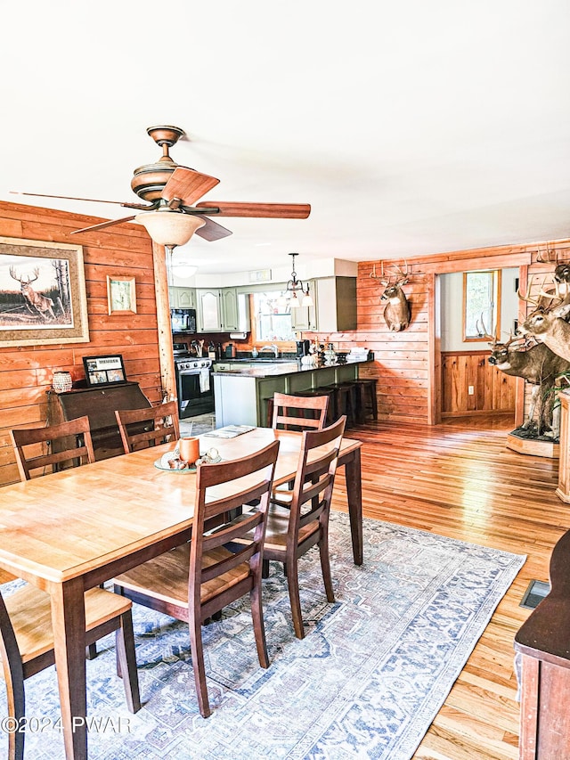 dining space with ceiling fan, light wood-type flooring, and wooden walls