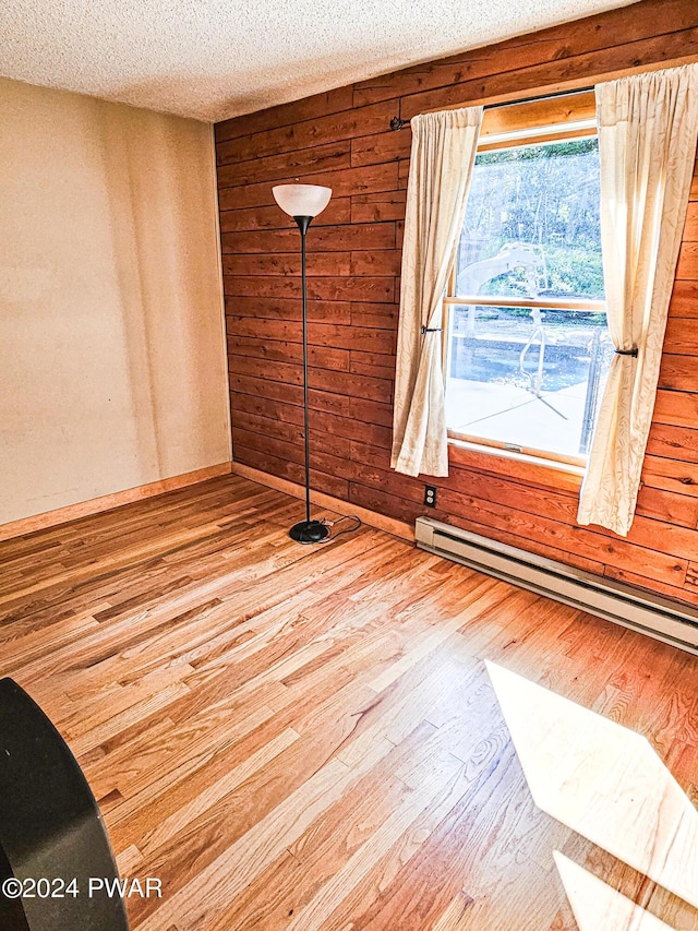 unfurnished room featuring a textured ceiling, hardwood / wood-style flooring, baseboard heating, and wood walls