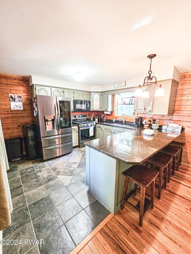 kitchen featuring kitchen peninsula, wooden walls, hanging light fixtures, and stainless steel appliances