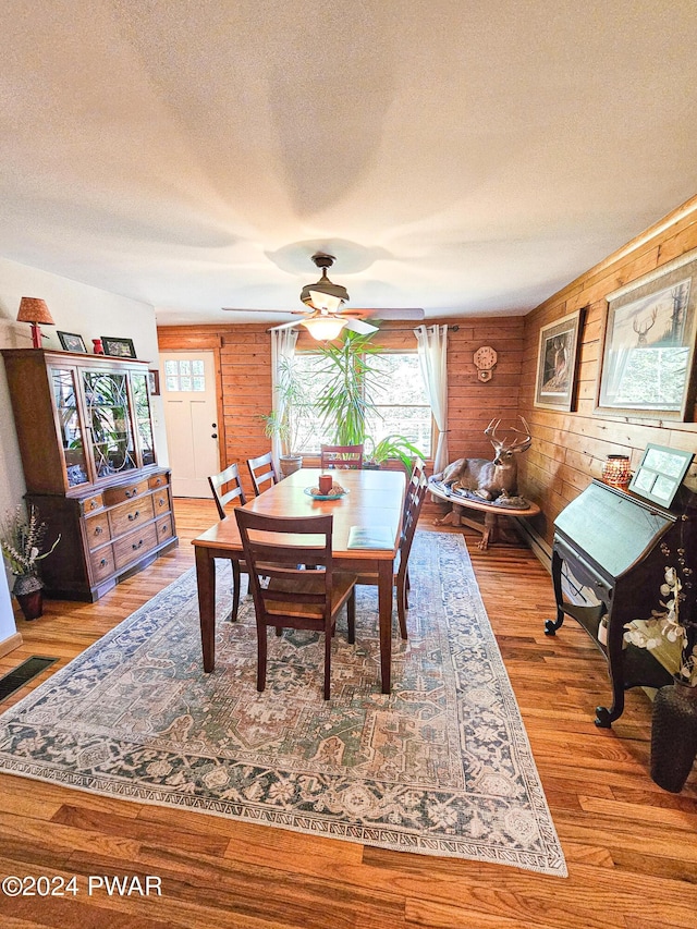 dining area featuring wooden walls, ceiling fan, light hardwood / wood-style floors, and a textured ceiling