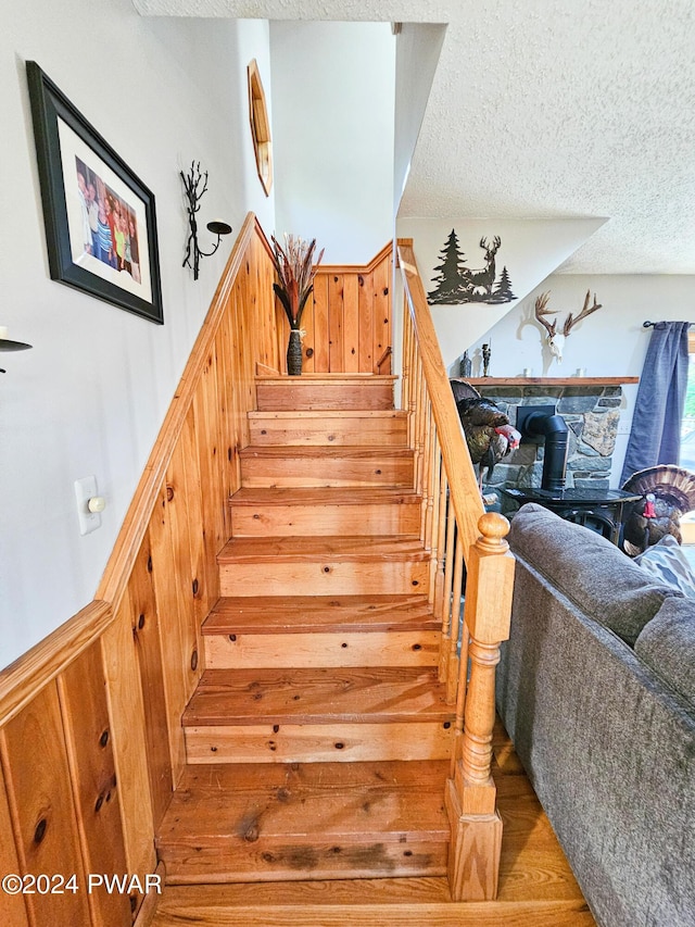 stairs with a textured ceiling and a wood stove