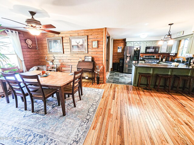 dining room featuring ceiling fan, wood walls, light wood-type flooring, and a wealth of natural light