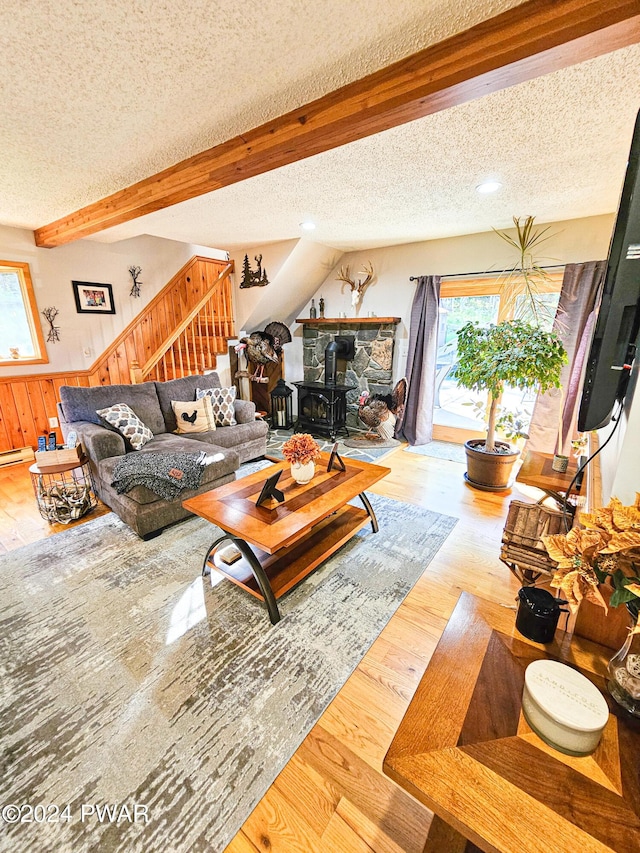 living room featuring beam ceiling, a wood stove, a textured ceiling, and hardwood / wood-style flooring