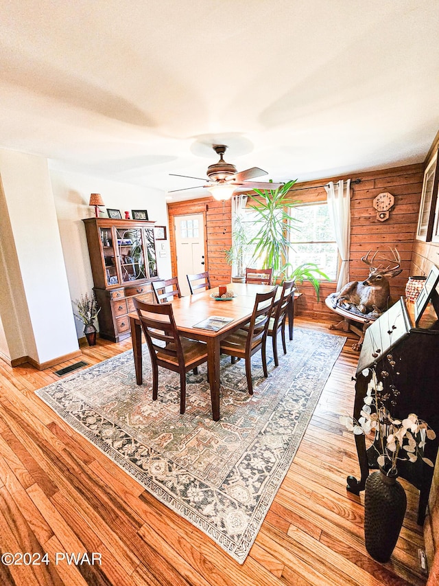 dining area with hardwood / wood-style floors, ceiling fan, and wood walls