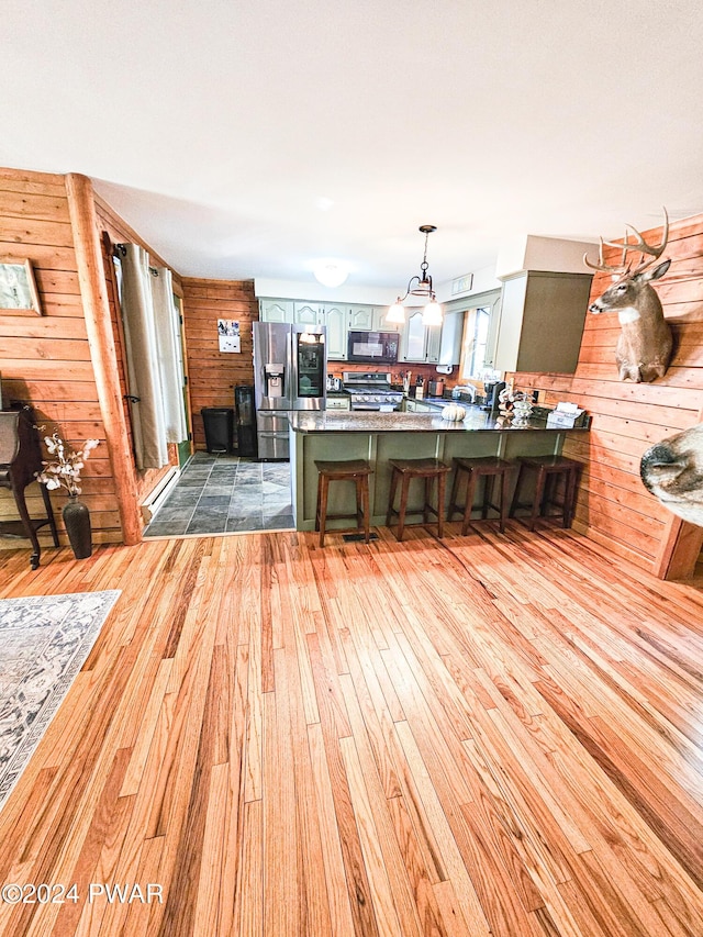 interior space featuring kitchen peninsula, appliances with stainless steel finishes, a kitchen breakfast bar, light hardwood / wood-style flooring, and wood walls