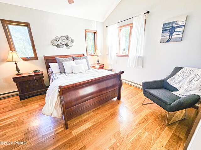 bedroom with ceiling fan, light hardwood / wood-style floors, a baseboard heating unit, and vaulted ceiling