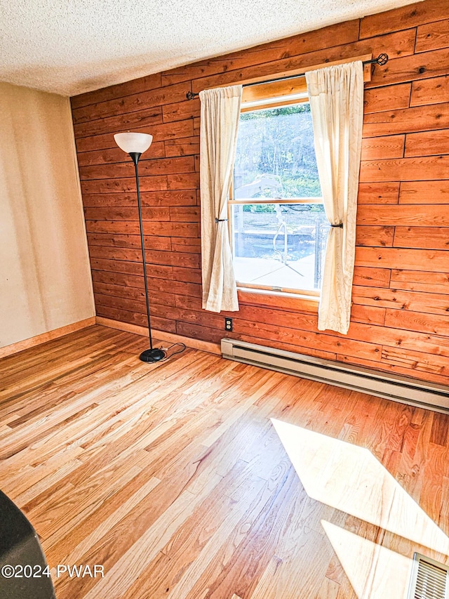 empty room with hardwood / wood-style flooring, wood walls, baseboard heating, and a textured ceiling