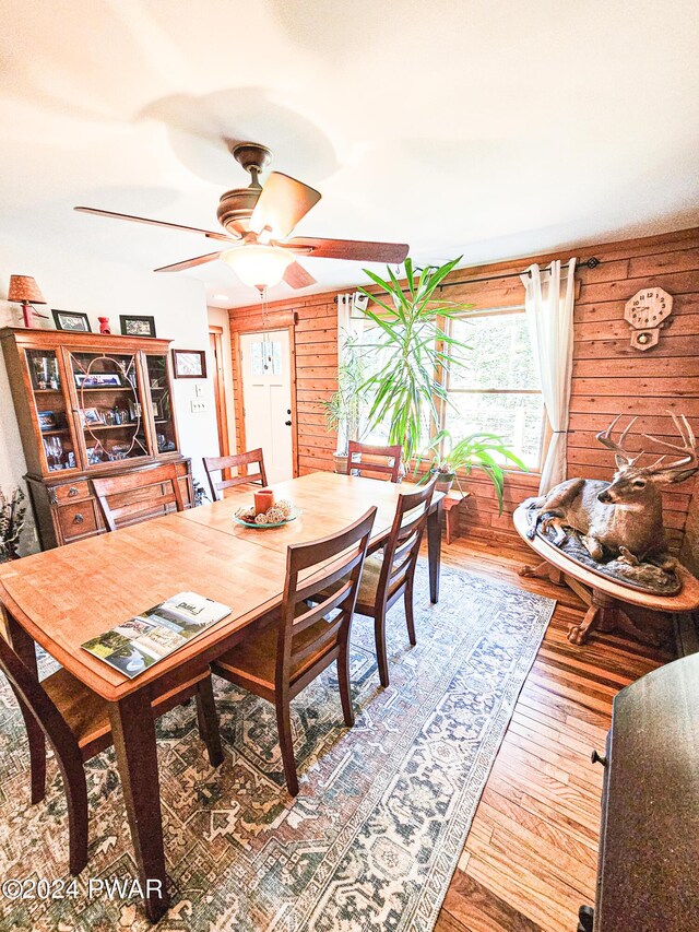 dining area with wooden walls, ceiling fan, and wood-type flooring