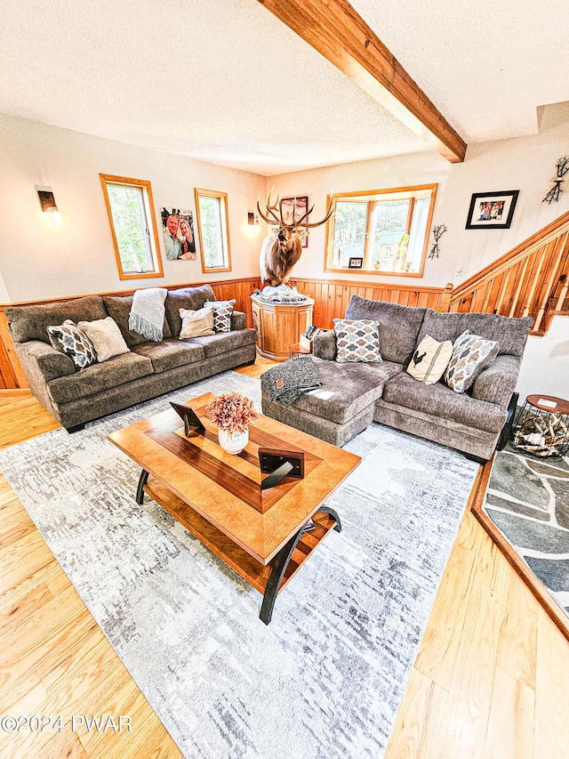 living room featuring beam ceiling, wood walls, wood-type flooring, and a textured ceiling