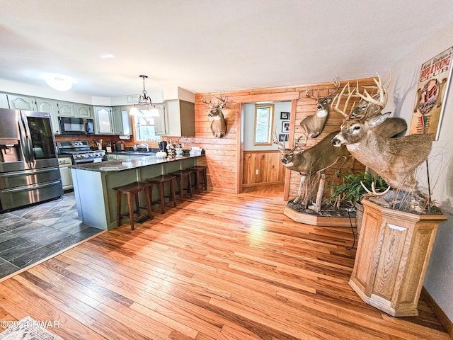 kitchen featuring kitchen peninsula, a kitchen breakfast bar, stainless steel appliances, sink, and wood walls