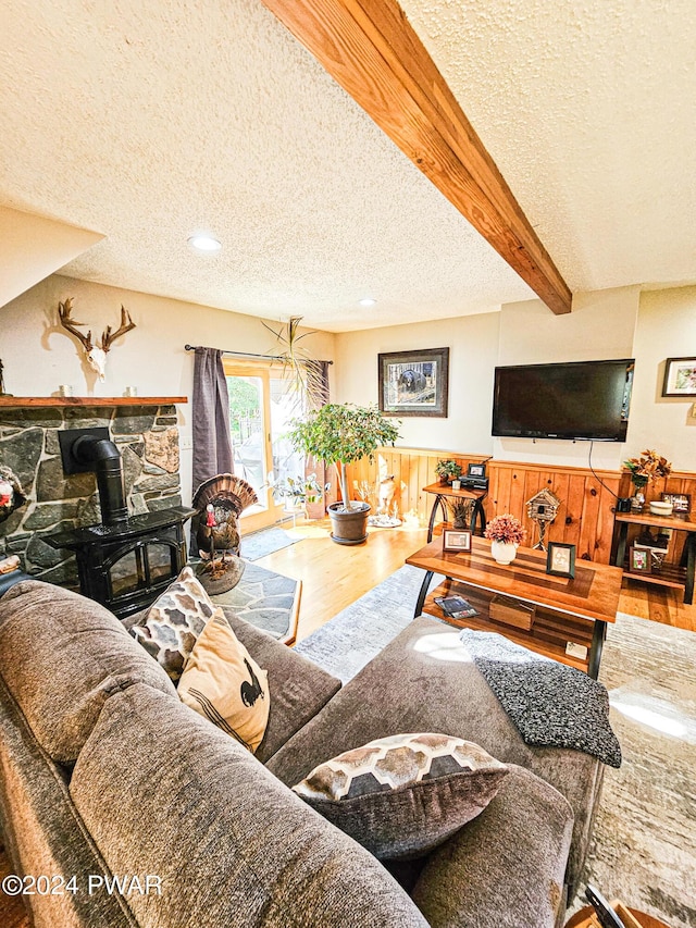 living room with beamed ceiling, a textured ceiling, hardwood / wood-style flooring, and a wood stove