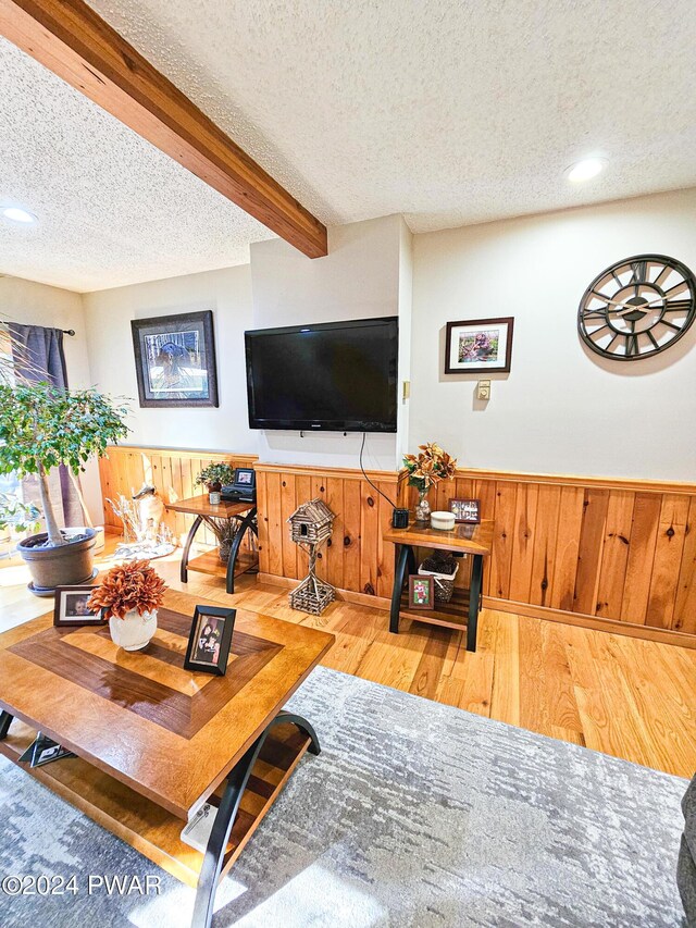 living room featuring wooden walls, hardwood / wood-style floors, beamed ceiling, and a textured ceiling