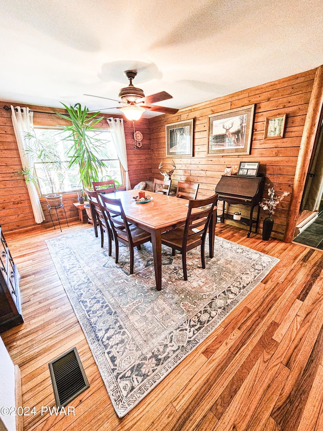 dining space with hardwood / wood-style flooring, ceiling fan, wood walls, and a textured ceiling