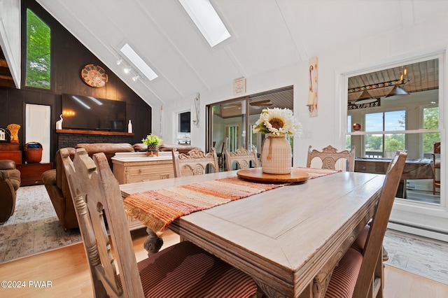 dining space with beam ceiling, a skylight, high vaulted ceiling, and light hardwood / wood-style floors