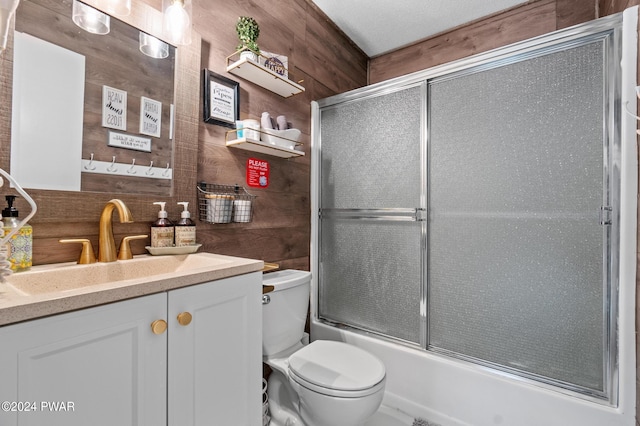 full bathroom with vanity, wood walls, toilet, and enclosed tub / shower combo