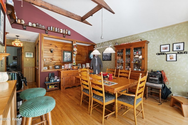 dining area with lofted ceiling with beams, wallpapered walls, and light wood finished floors