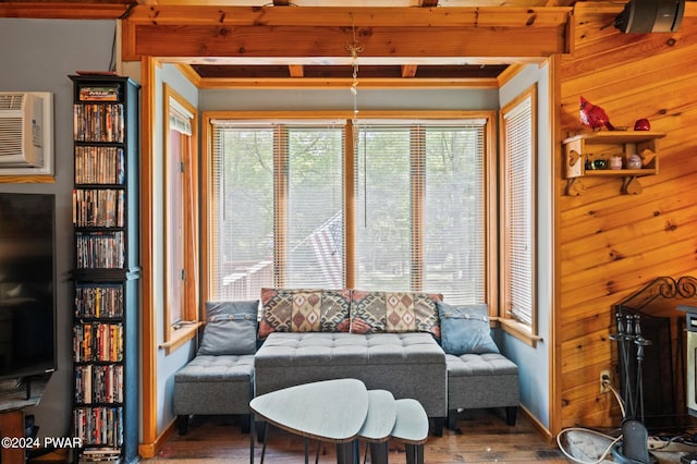 living room featuring baseboards, wooden walls, beam ceiling, and wood finished floors