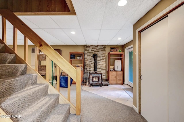 stairs featuring a wood stove, a paneled ceiling, and carpet flooring