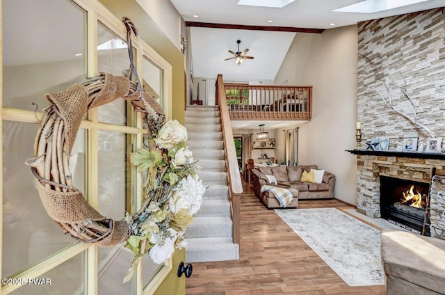 living room featuring a skylight, light hardwood / wood-style flooring, a towering ceiling, ceiling fan, and a fireplace