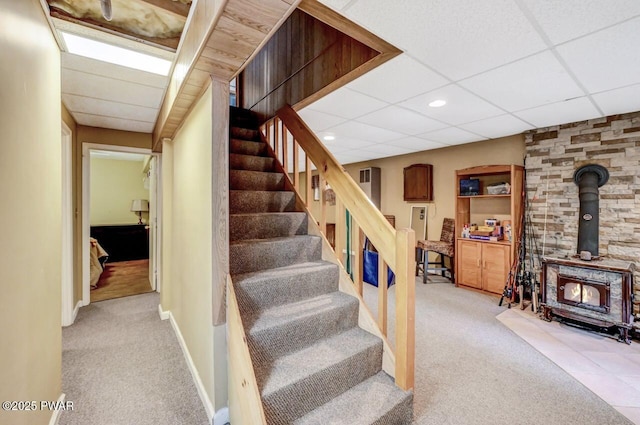 stairs featuring carpet flooring, a paneled ceiling, and a wood stove