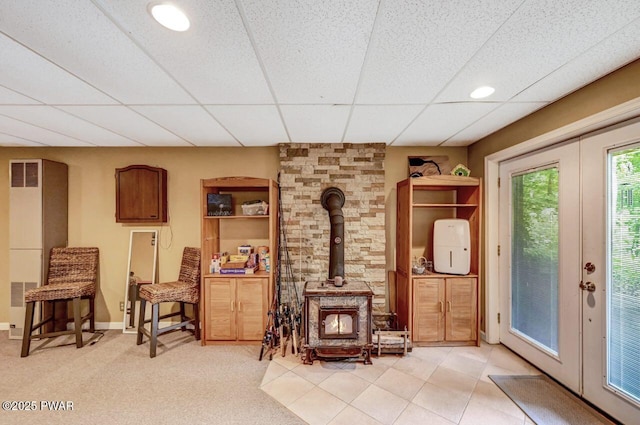 living area featuring a paneled ceiling, light colored carpet, french doors, and a wood stove