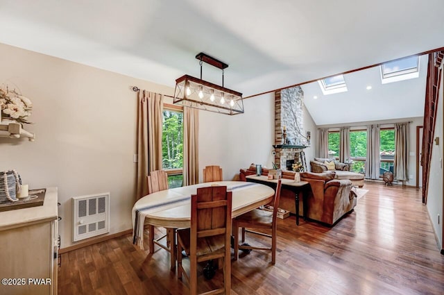 dining room with dark wood-type flooring, a fireplace, a chandelier, and lofted ceiling with skylight