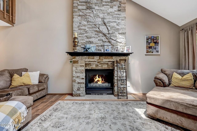 living room featuring vaulted ceiling, a stone fireplace, and light wood-type flooring