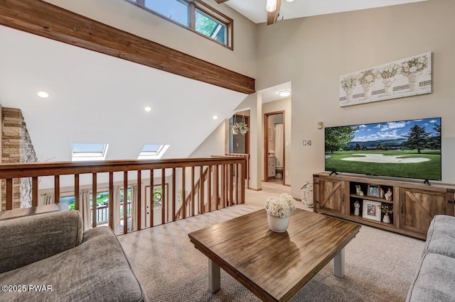 living room featuring ceiling fan, beam ceiling, a skylight, high vaulted ceiling, and light carpet