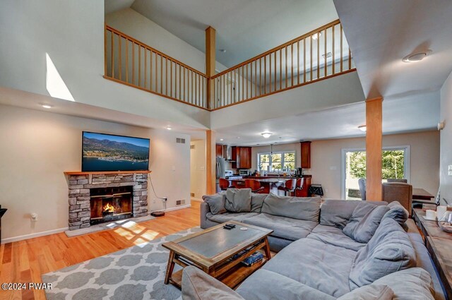 living room with light wood-type flooring, a towering ceiling, and a stone fireplace