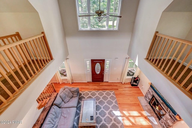 living room with light wood-type flooring, a towering ceiling, ceiling fan, and a fireplace