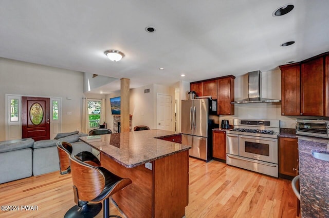 kitchen with a breakfast bar, wall chimney range hood, a kitchen island, light hardwood / wood-style floors, and stainless steel appliances