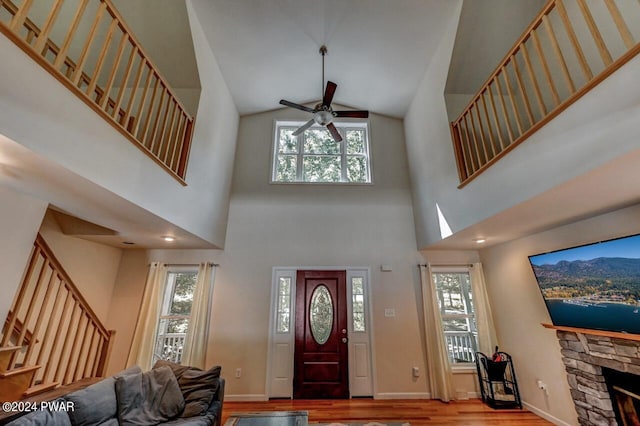 entrance foyer featuring a high ceiling, light wood-type flooring, a stone fireplace, and plenty of natural light