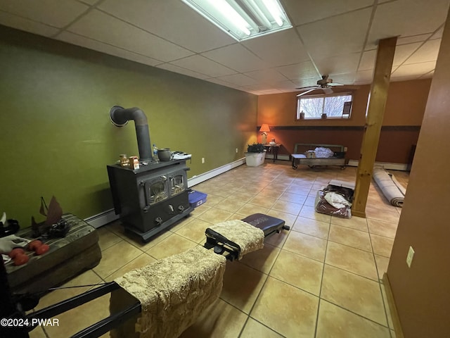 living room with a wood stove, ceiling fan, a paneled ceiling, and a baseboard radiator