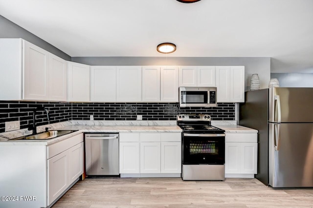 kitchen with light stone countertops, appliances with stainless steel finishes, backsplash, sink, and white cabinets