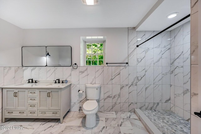 bathroom with a tile shower, vanity, tile walls, and toilet