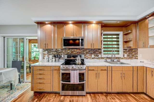 kitchen with light stone countertops, sink, backsplash, appliances with stainless steel finishes, and light wood-type flooring