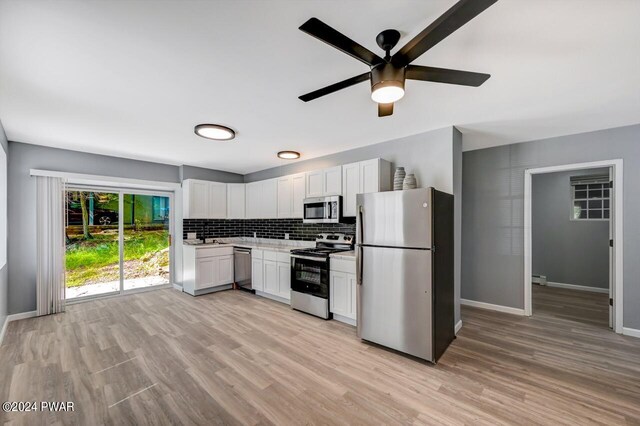 kitchen with backsplash, white cabinets, stainless steel appliances, and light hardwood / wood-style floors